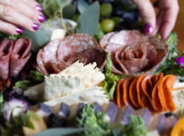 a woman's hands working on creating a charcuterie spread that includes meats and cheeses